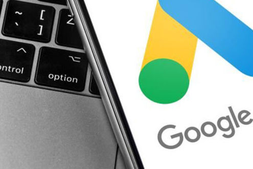 Mobile phone displaying the Google Ads logo with a laptop in the background