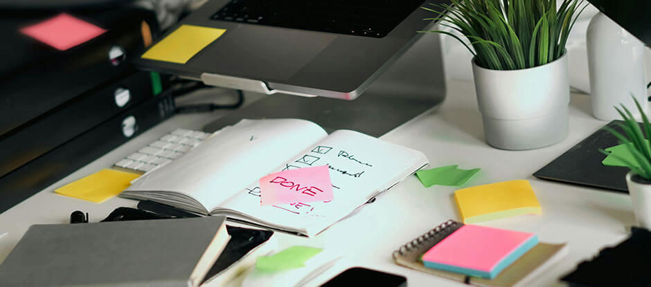 A cluttered desk with post it notes and checklists