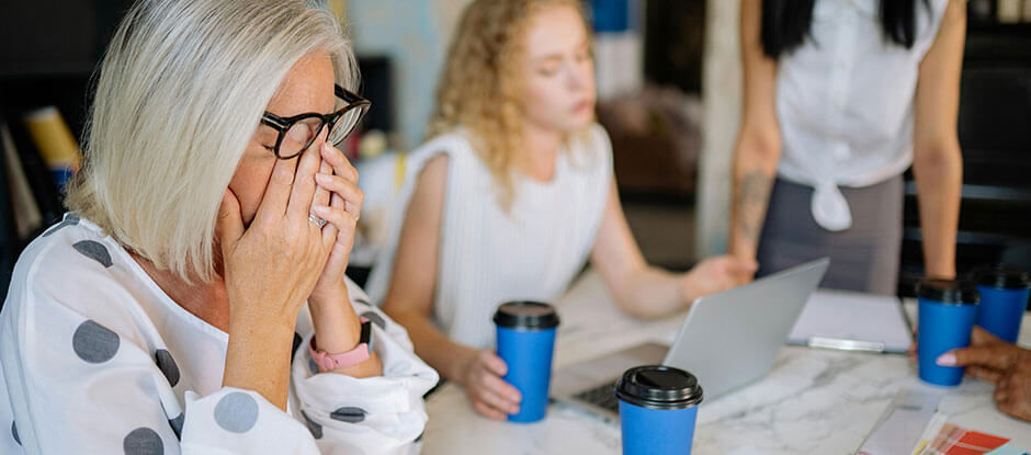 3 females visibly stressed from the project they are working on with coffee cups on a able