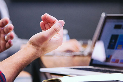 Hands gesturing with a laptop and notepad on the desk
