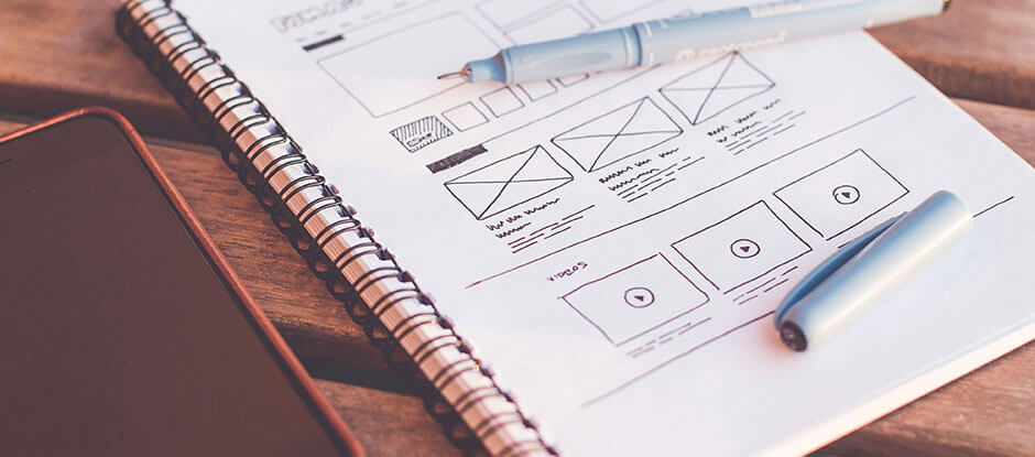 Notepad with a pen with a website wireframe on the paper with a phone